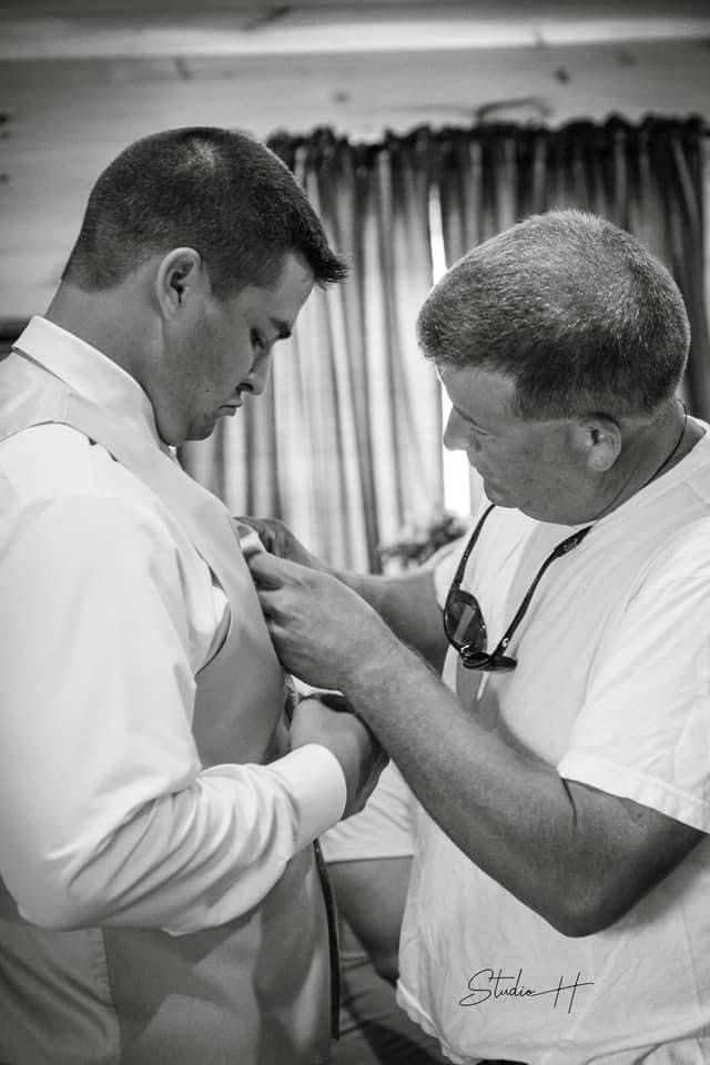 Father helps son with tie getting dressed for his wedding ceremony