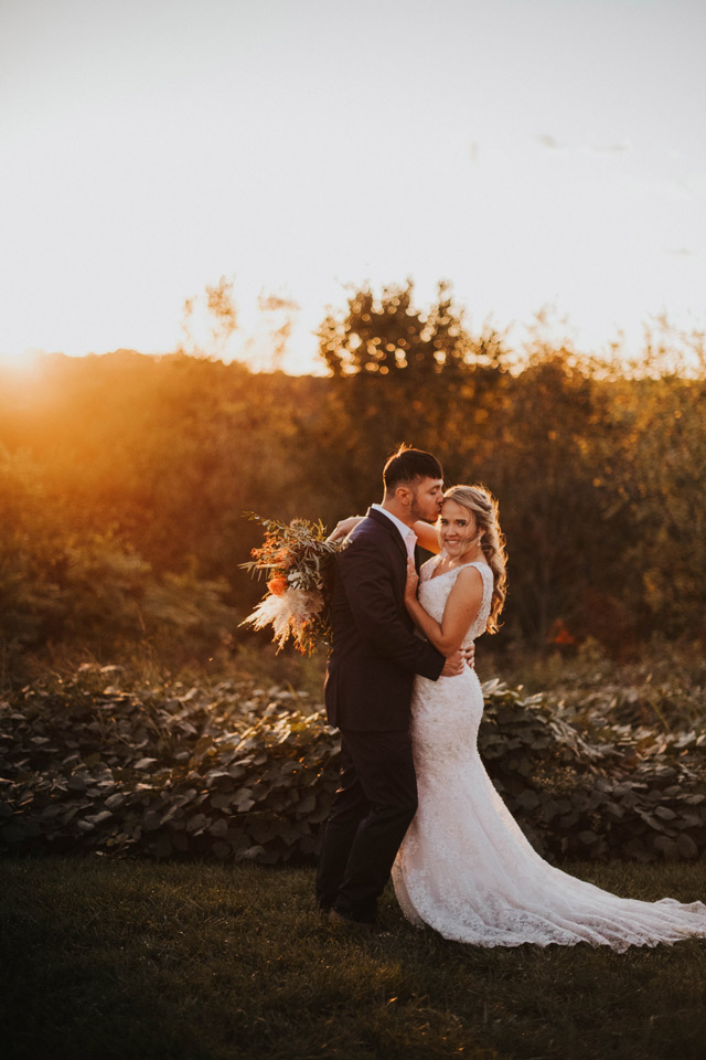 Happy newlyweds embrace as the sun sets in the distance on their wedding day