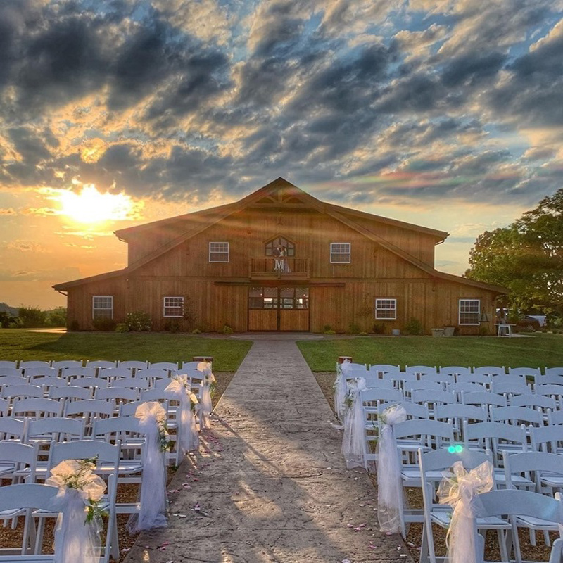View from the wedding ceremony site looking back at Homeplace venue across seating with sun setting and dramatic clouds and sunbeams